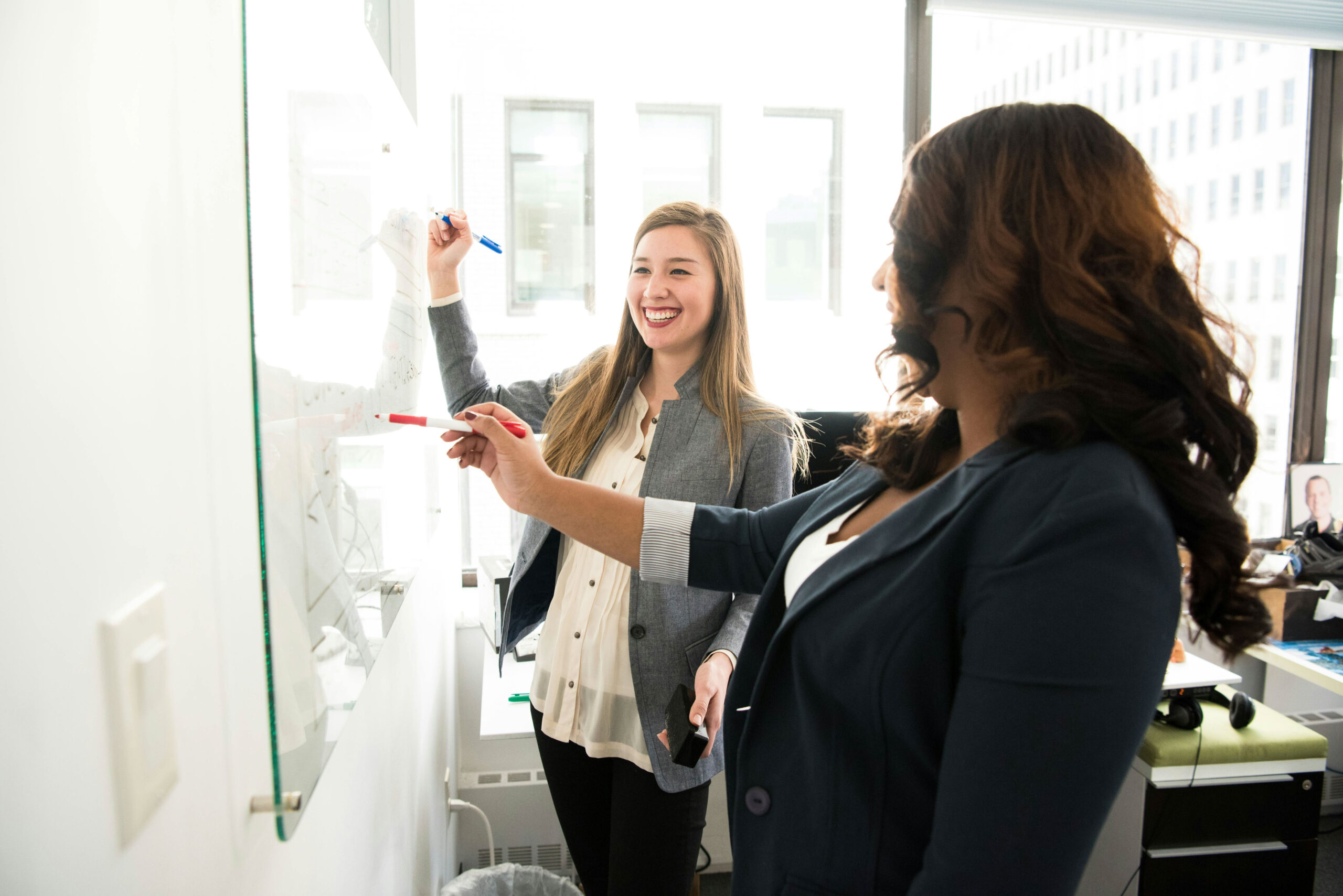 Junior and senior staff members work together at a white board on investment due diligence.