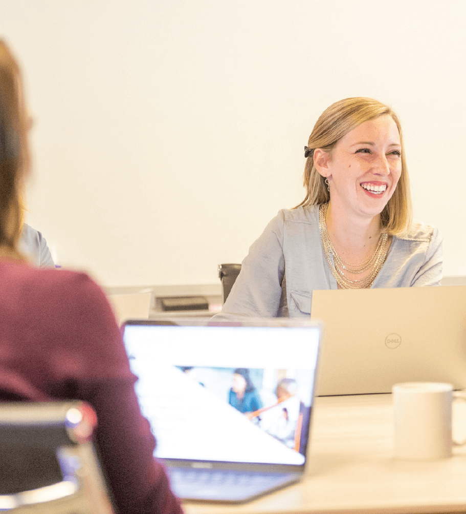 2 smiling employees sitting behind laptops