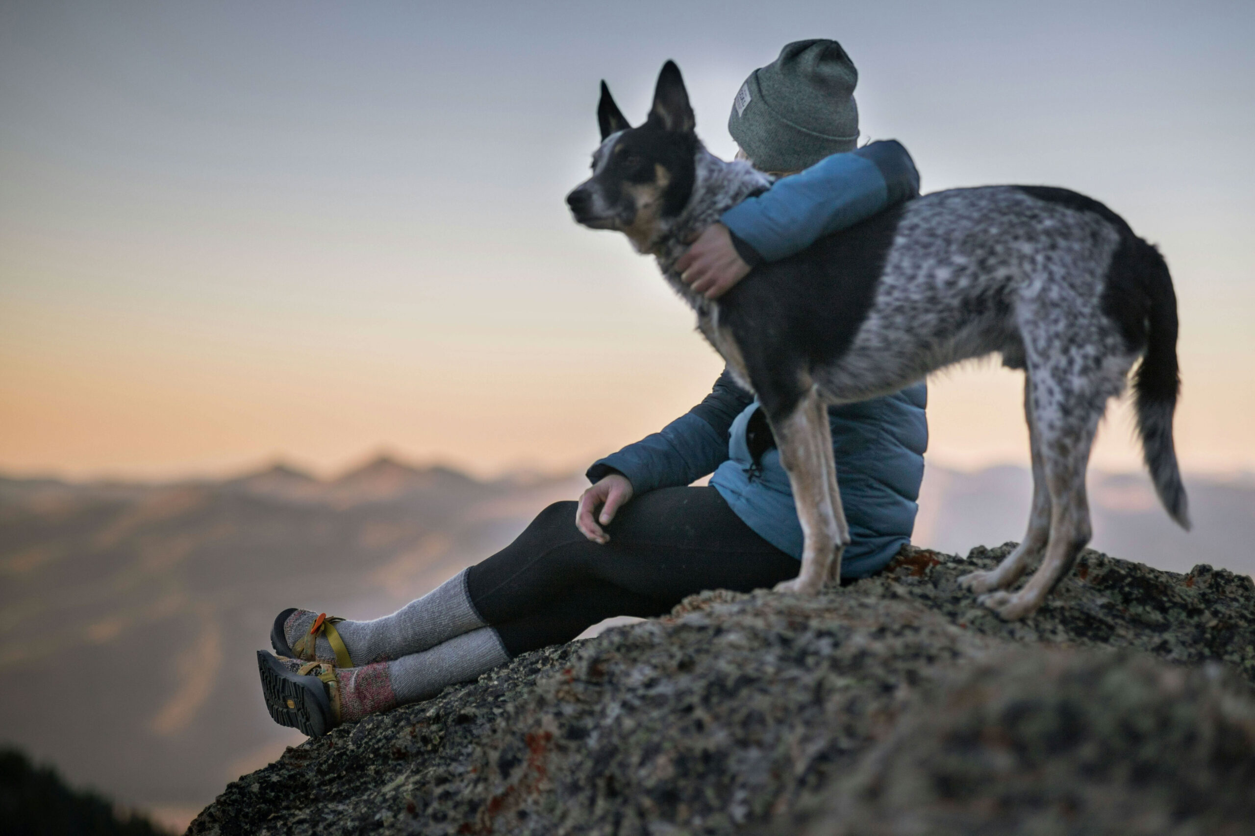 A solo hiker hugs her canine companion at the summit.