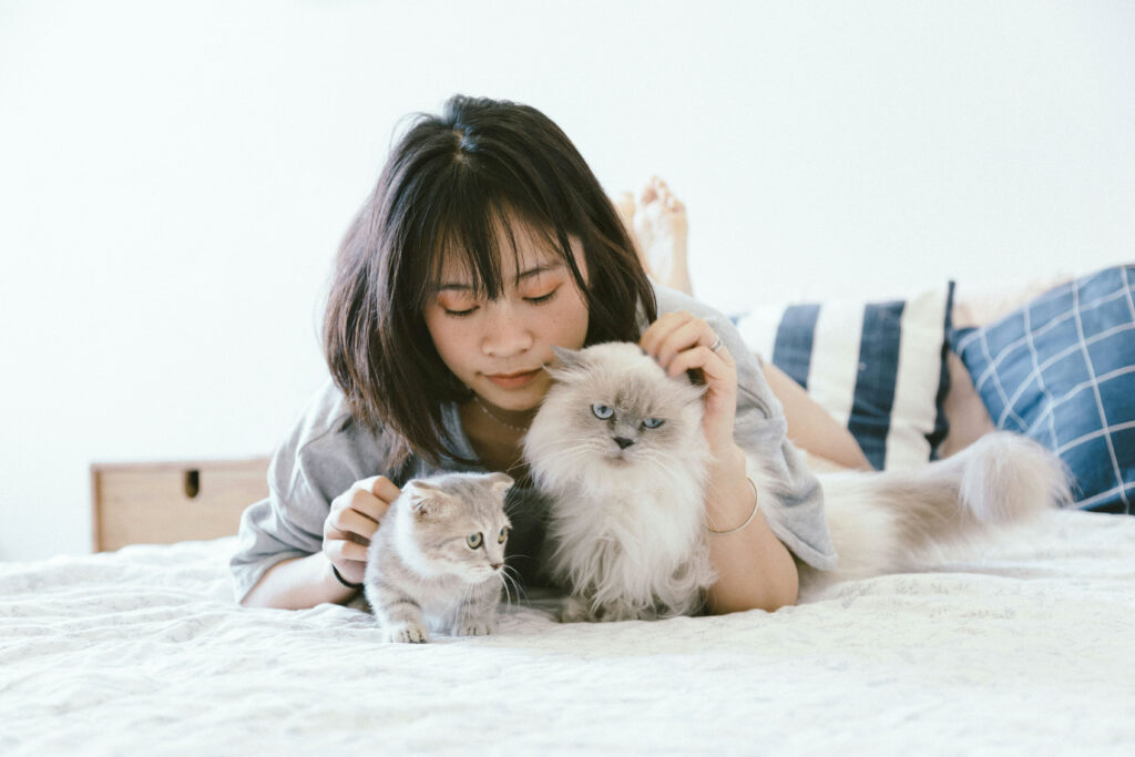 A young cat owner cuddles with her two cats, showcasing growing pet industry trends.