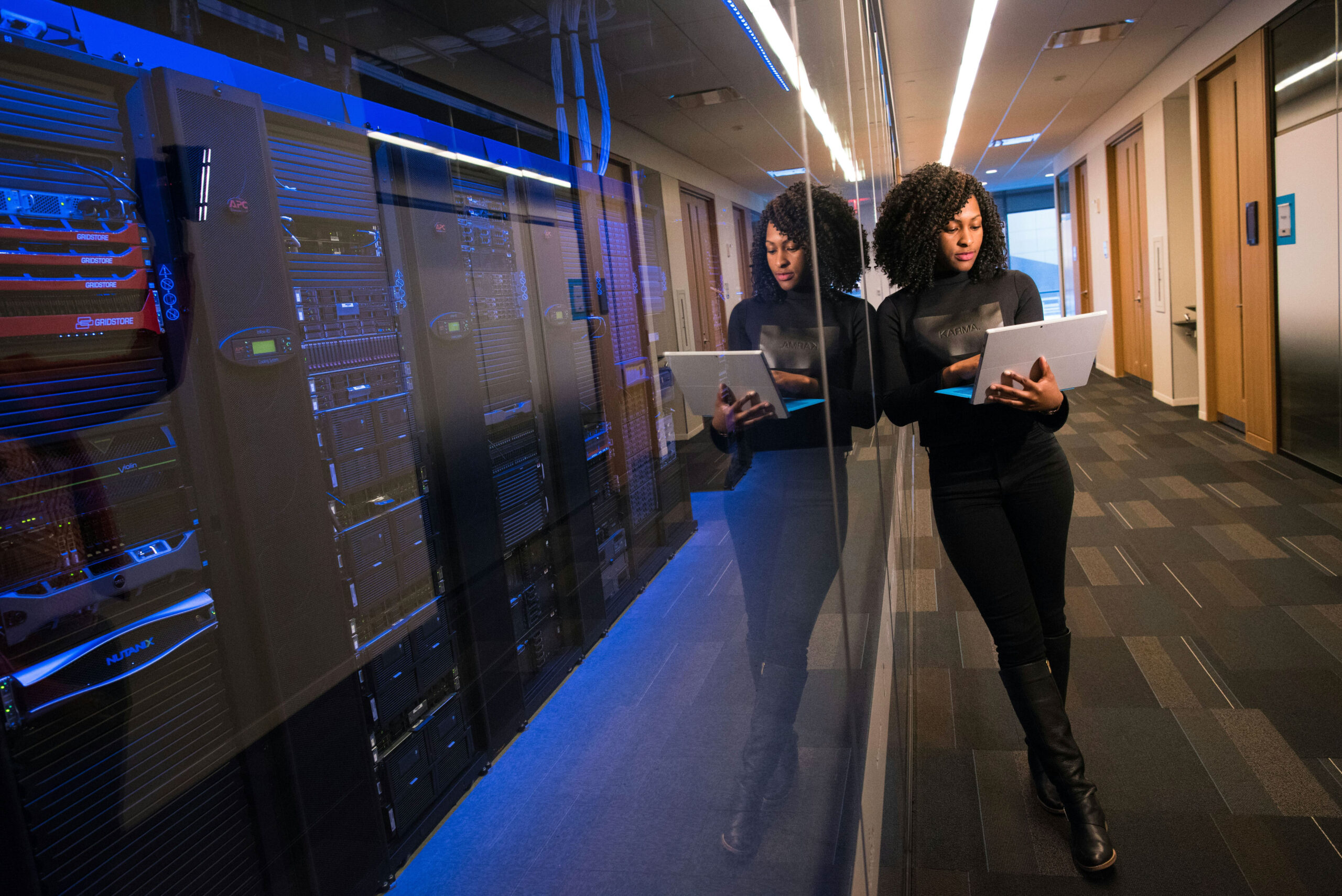 A black woman works on it due diligence while standing in front of server room.