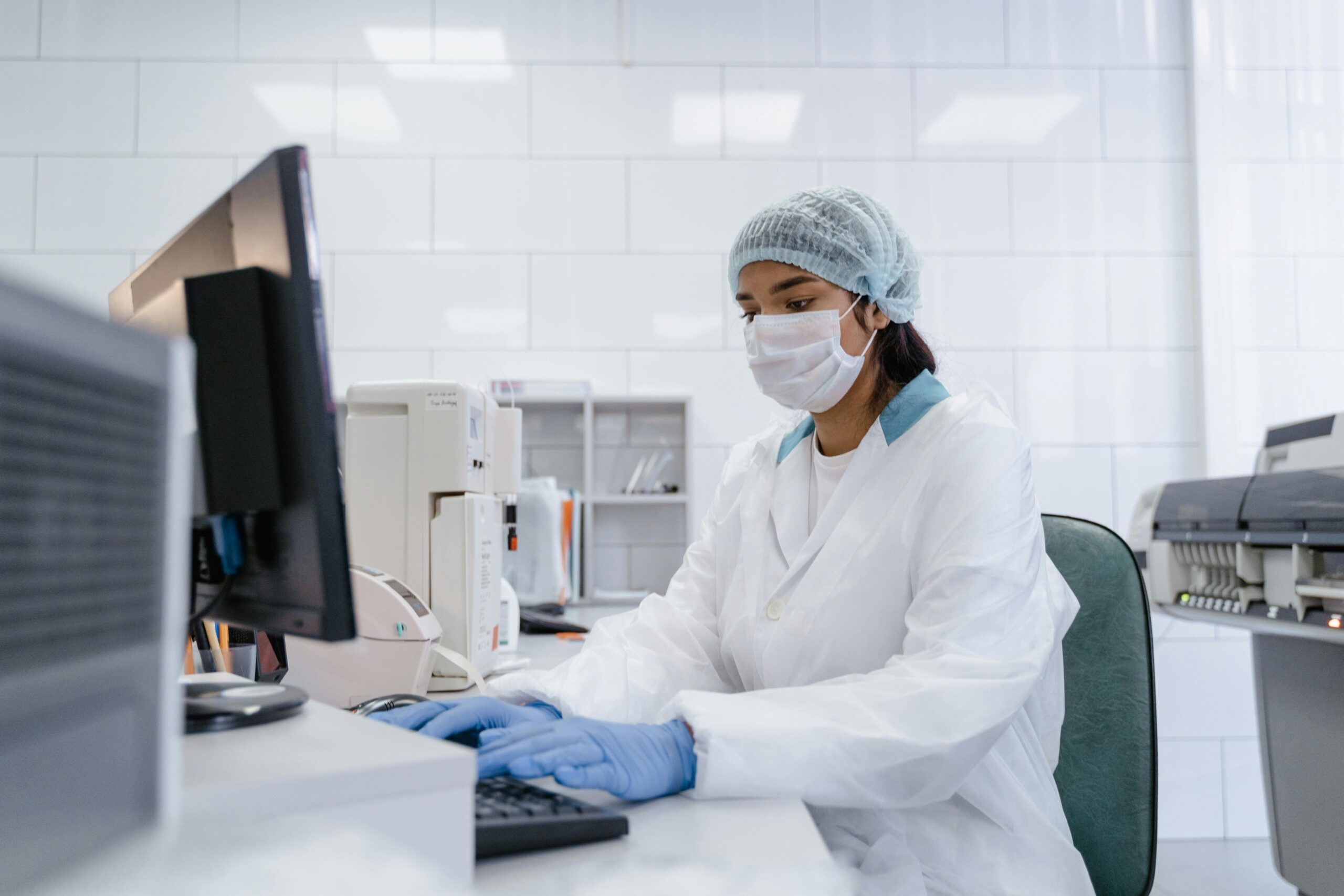 A scientist with wearing a medical mask sitting at a computer in a lab.