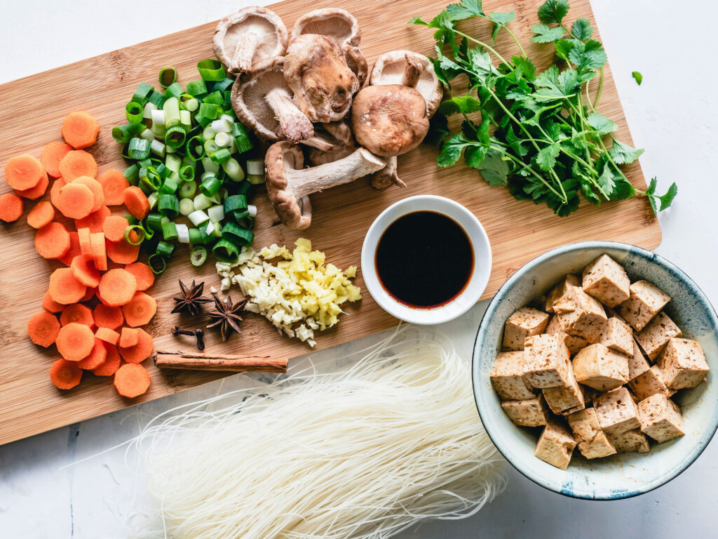 A spread of different foods and ingredients including mushrooms, chopped carrots, and a bowl of tofu.