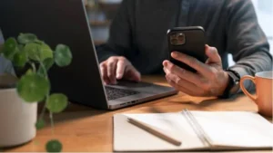 person sitting at laptop with phone and notebook